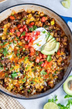 A skillet filled with a beef and bean mixture and topped with sour cream, tomatoes, and sliced avocado.