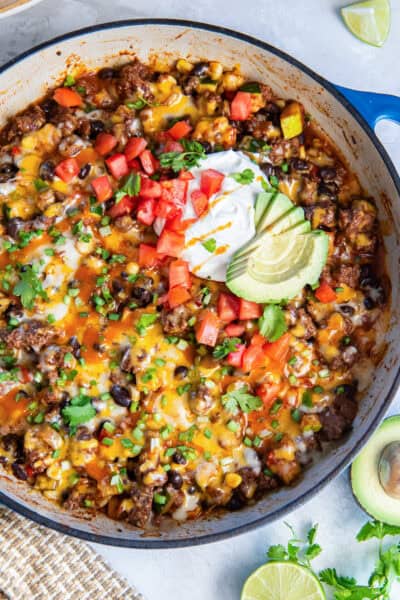 A skillet filled with a beef and bean mixture and topped with sour cream, tomatoes, and sliced avocado.