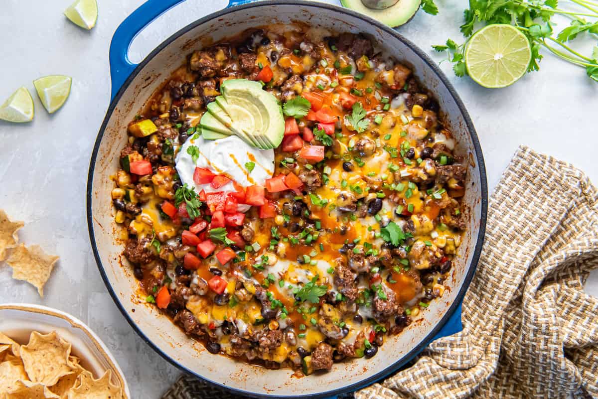 A loaded taco skillet topped with sour cream surrounded by lime wedges and tortilla chips.