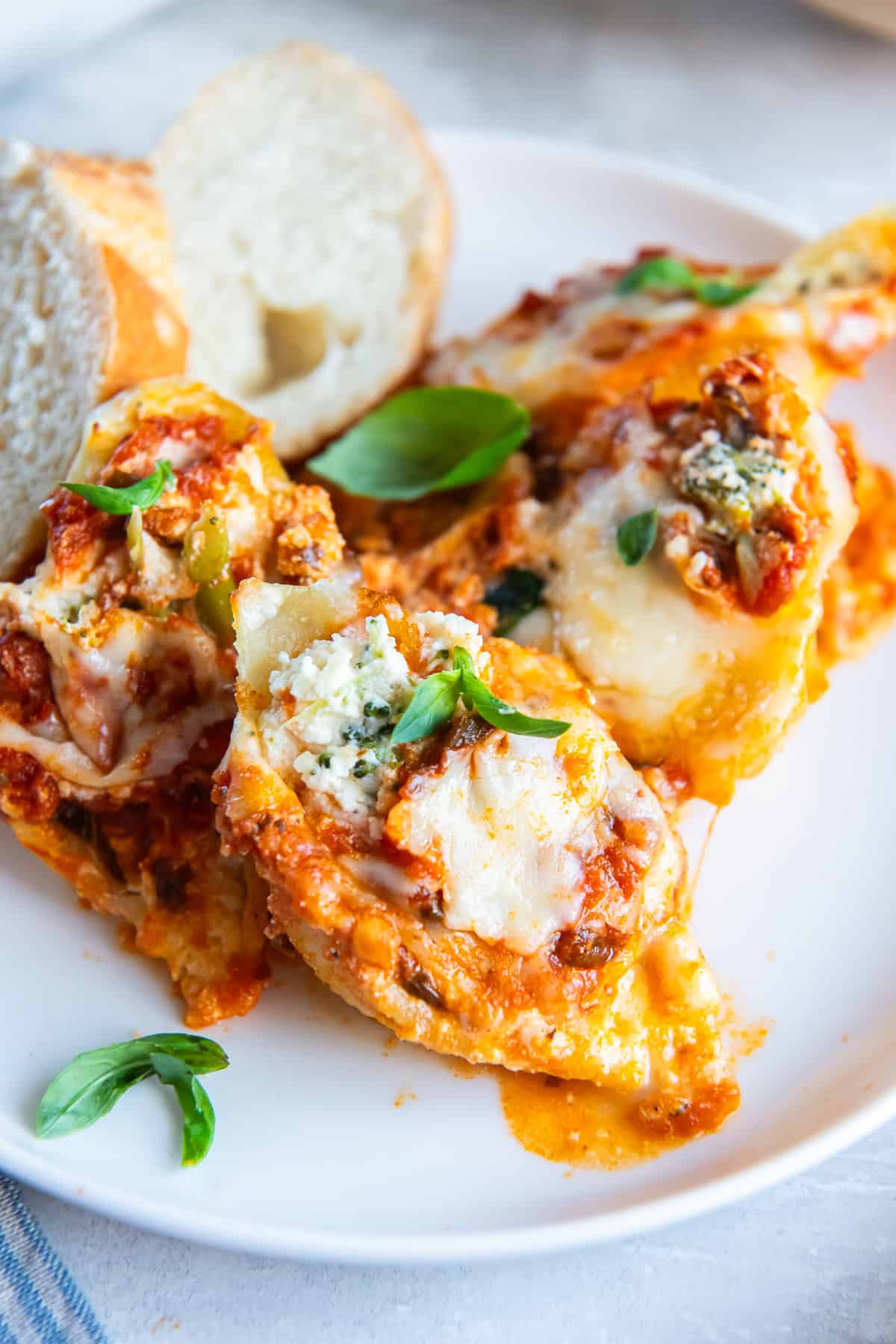 Three pasta shells stuffed with broccoli and cheese with marinara on a white dinner plate.