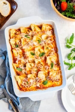 Broccoli cheese stuffed shells in a casserole dish on a dinner table with a salad and bread.