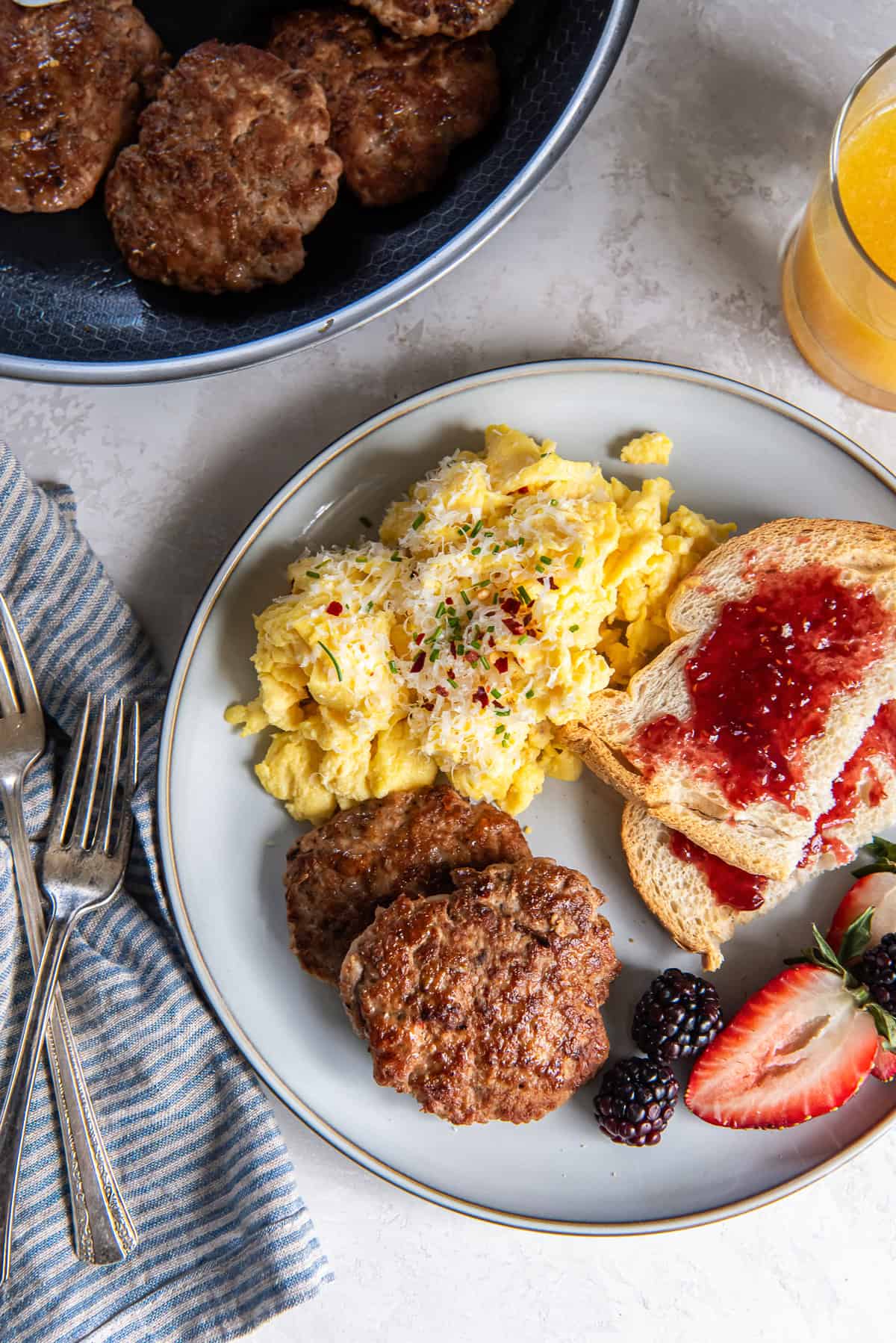Two turkey breakfast sausage patties on a plate with scrambled eggs and toast with jelly.
