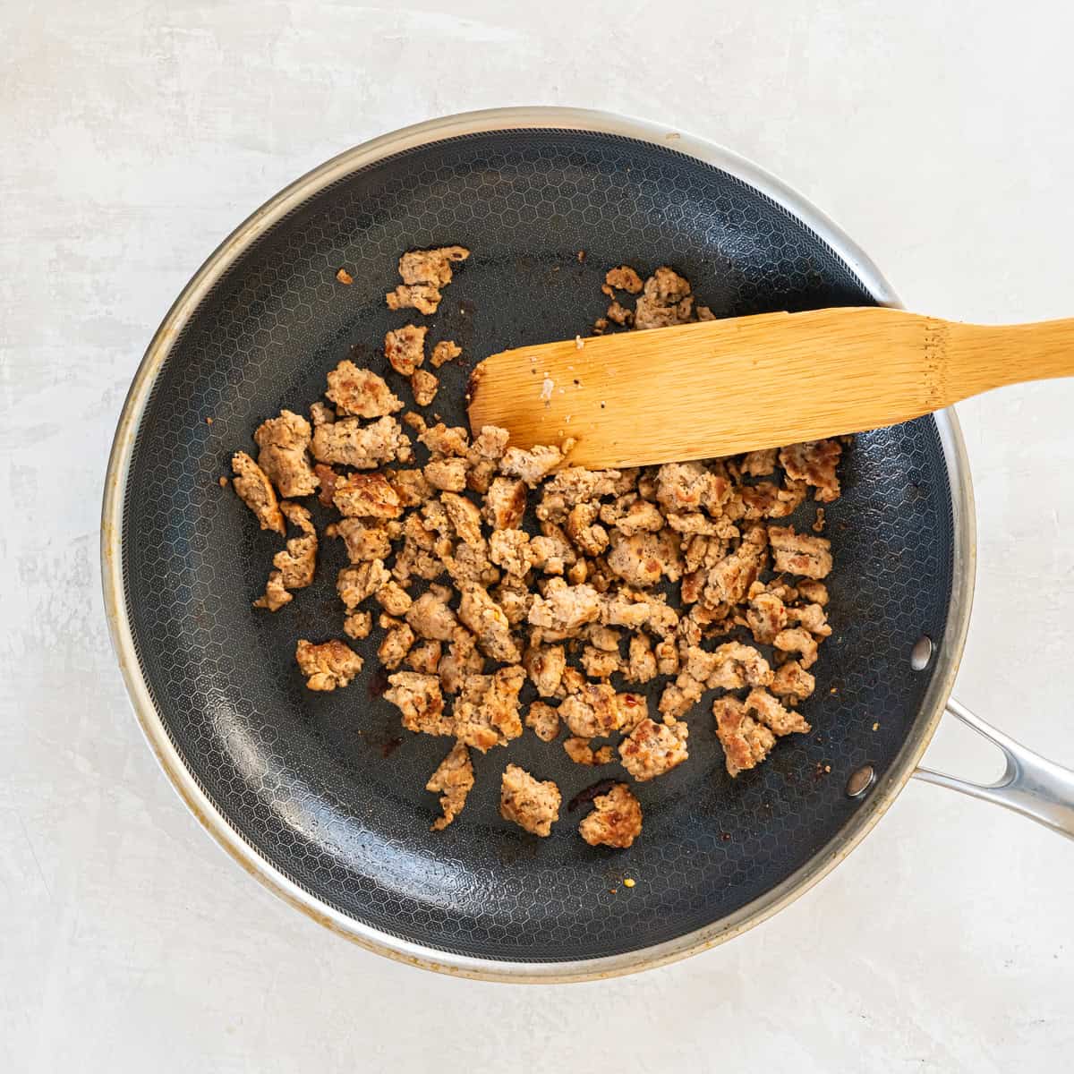 Crumbled turkey breakfast sausage in a skille with a wooden spoon.