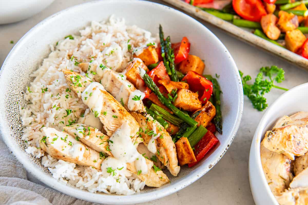 A white bowl filled with rice, chicken tenderloins, and roasted vegetables.