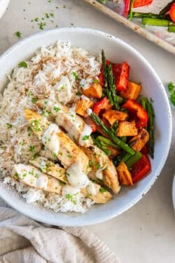 A bowl with rice, chicken tenderloins, and roasted vegetables.
