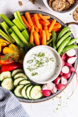 A platter of vegetables with a small bowl of cottage cheese dip garnished with fresh dill.