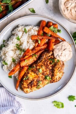 Spiced chicken and roasted carrots on a plate with a dipping sauce and rice.