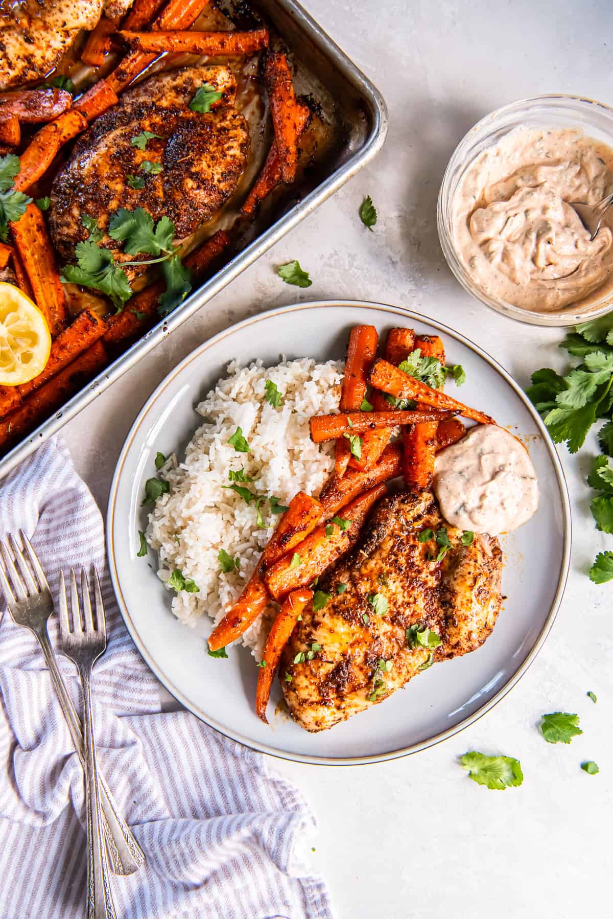 Chicken and roasted carrots on a plate with rice and a small bowl of dipping sauce.