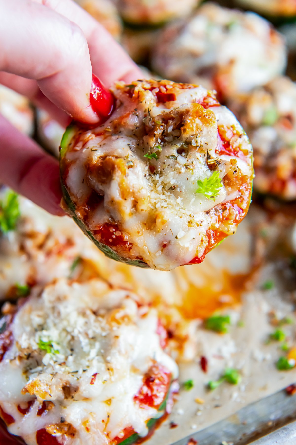 A hand holding a zucchini pizza bite.
