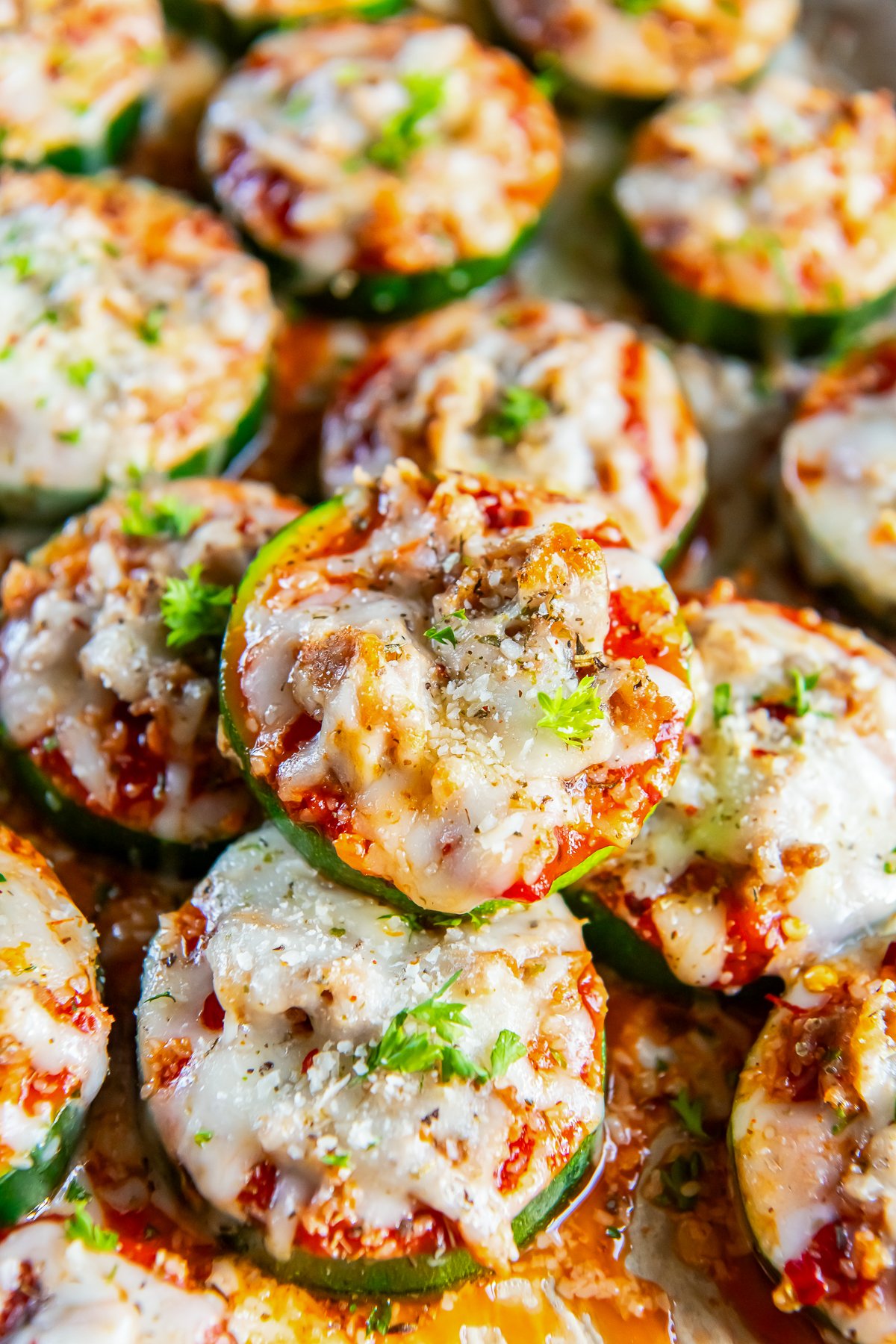 A pile of mini zucchini pizzas with italian sausage and melted cheese.