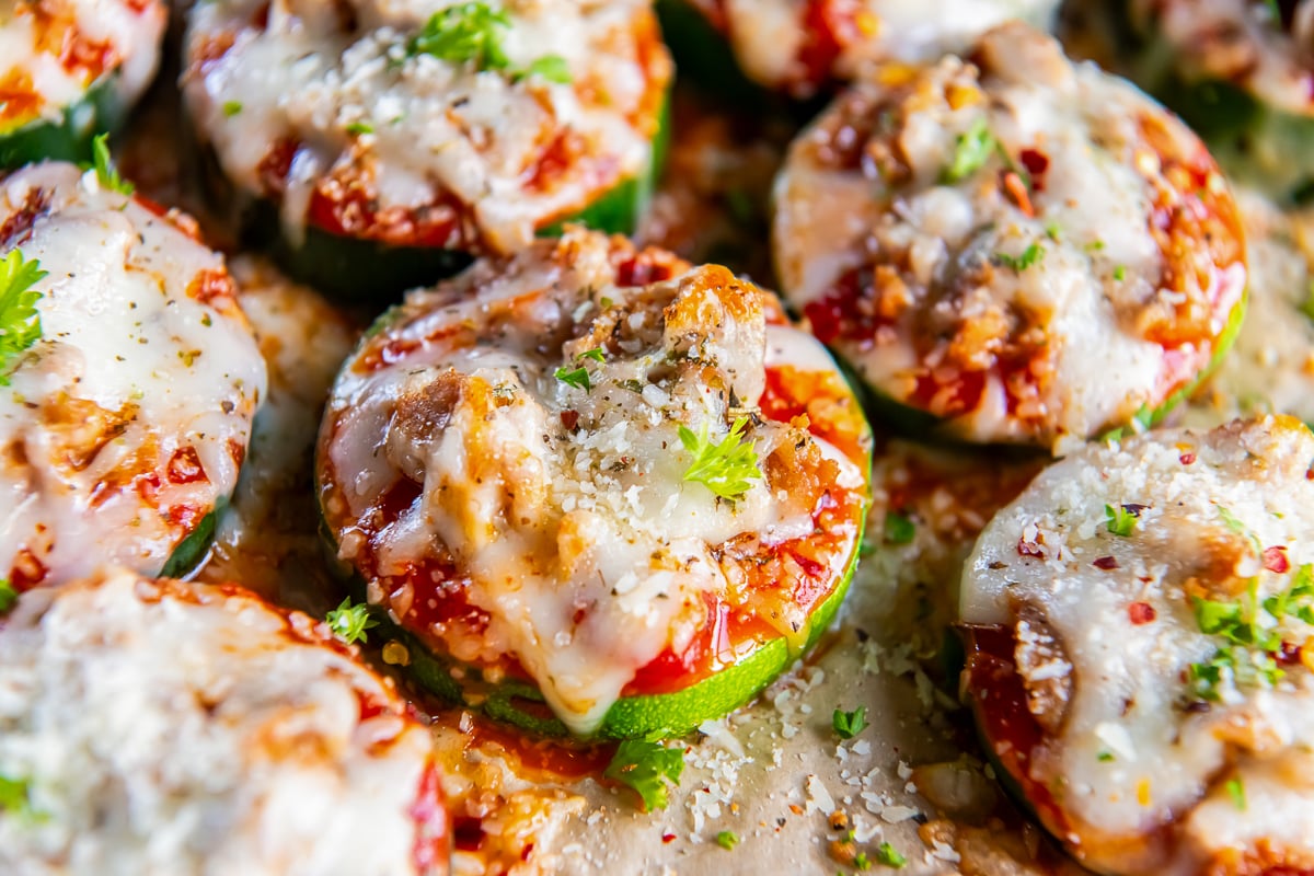 A pile of mini zucchini pizzas with italian sausage and melted cheese.