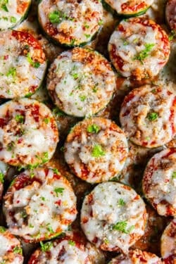 Zucchini pizzas with sausage and cheese on a baking sheet.