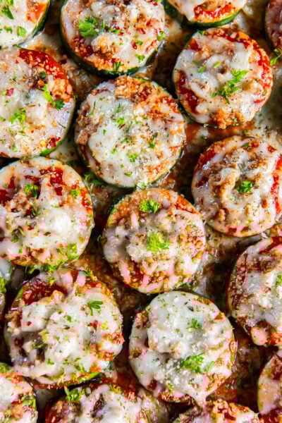 Zucchini pizzas with sausage and cheese on a baking sheet.