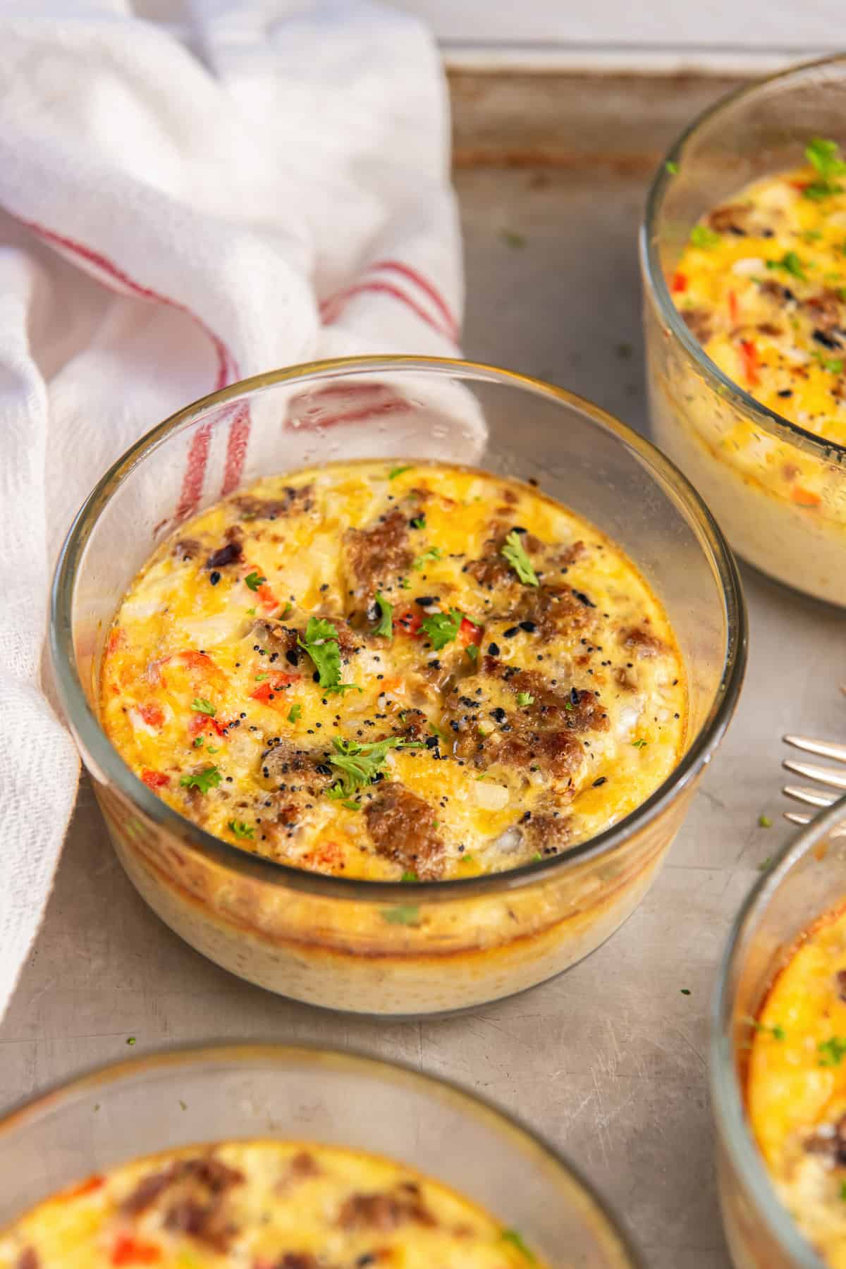 Egg bakes with sausage and cheese in glass containers on a baking sheet.