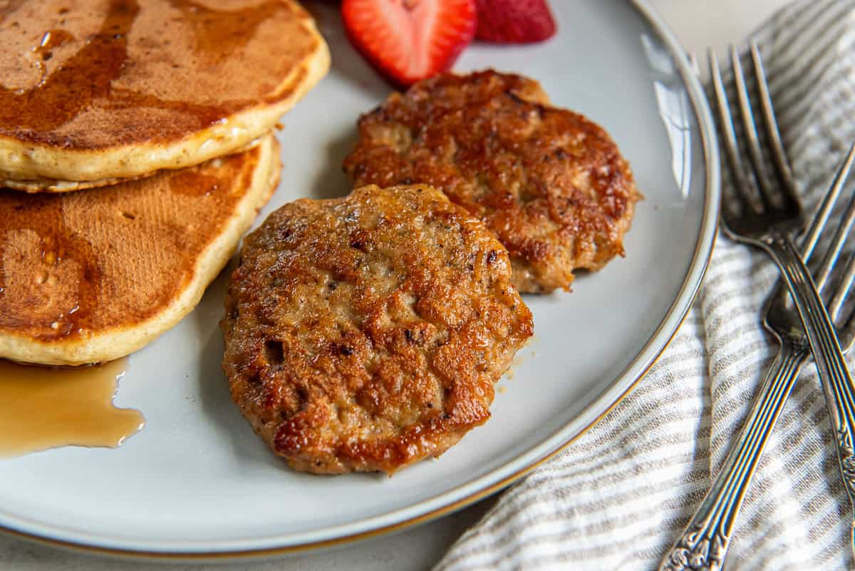 Two chicken breakfast sausage patties on a plate with pancakes and strawberries.
