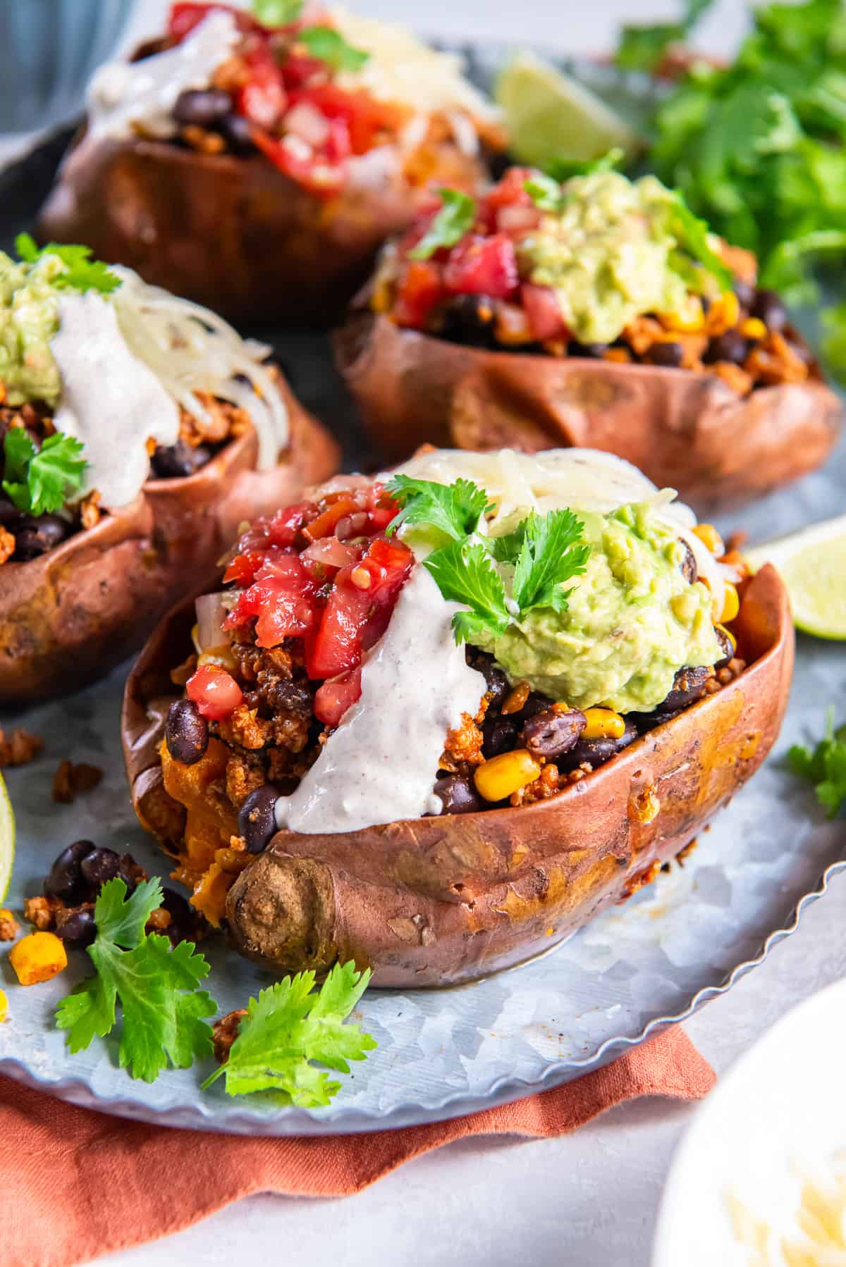 A baked sweet potato stuffed with taco filling, corn, black beans and garnished with a creamy sauce, salsa, and guacamole.