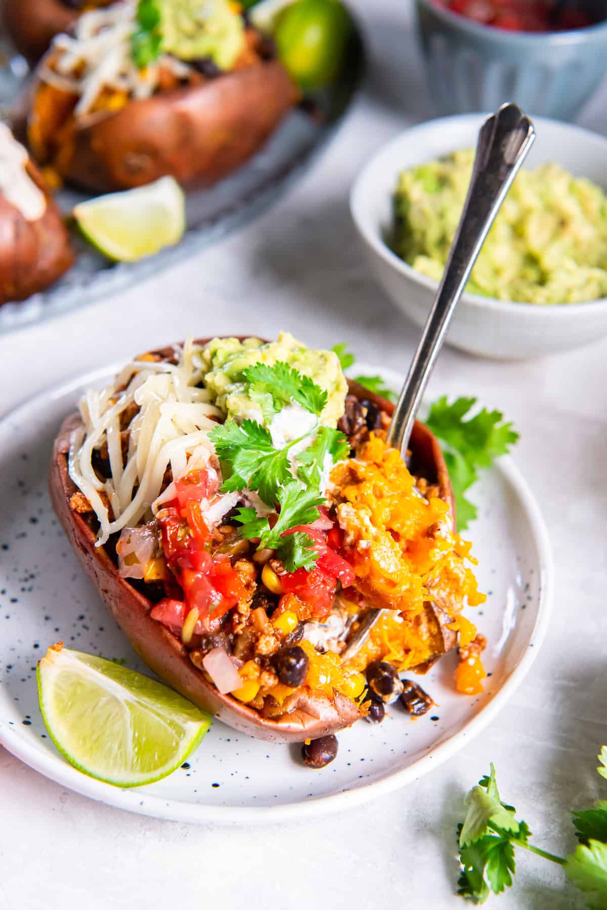 A fork digging into a taco stuffed sweet potato on a white plate with a lime wedge next to it.