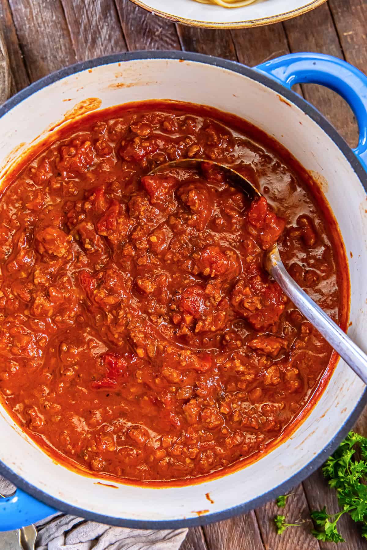 Chicken bolognese in a Dutch oven with a ladle, ready to serve.