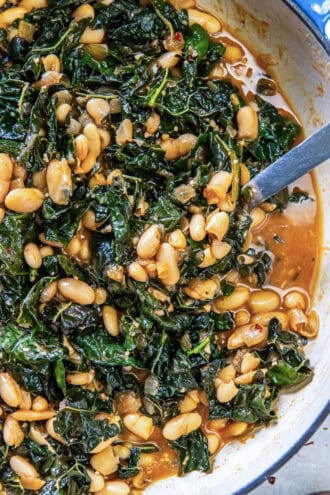A spoon resting in a skillet of braised white beans and greens.
