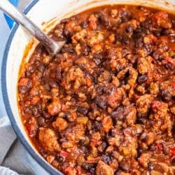 A spoon resting in a pot of turkey black bean chili with rich red sauce and hearty mix of beans, turkey, and vegetables.