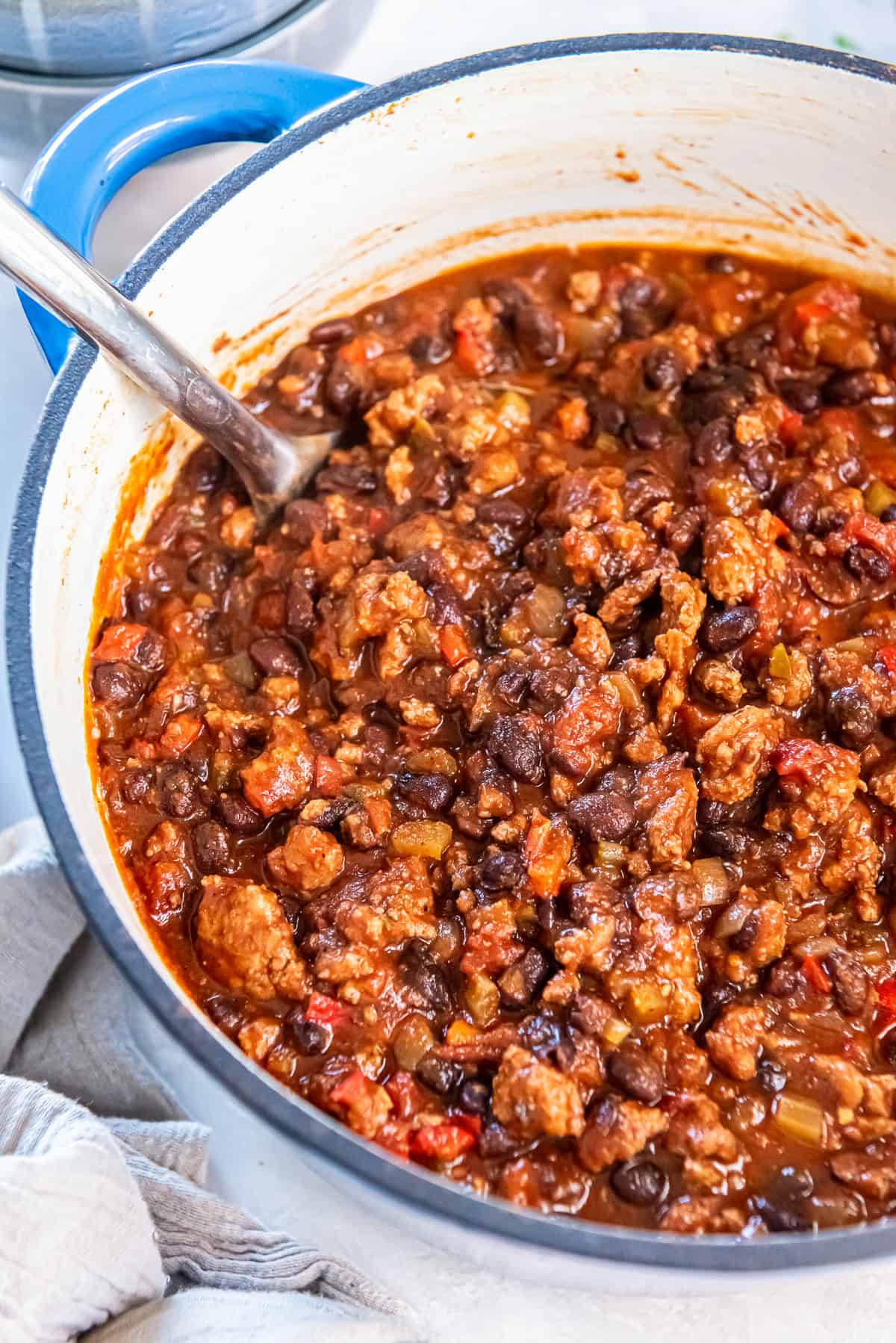 A spoon resting in a pot of turkey black bean chili with rich red sauce and hearty mix of beans, turkey, and vegetables.