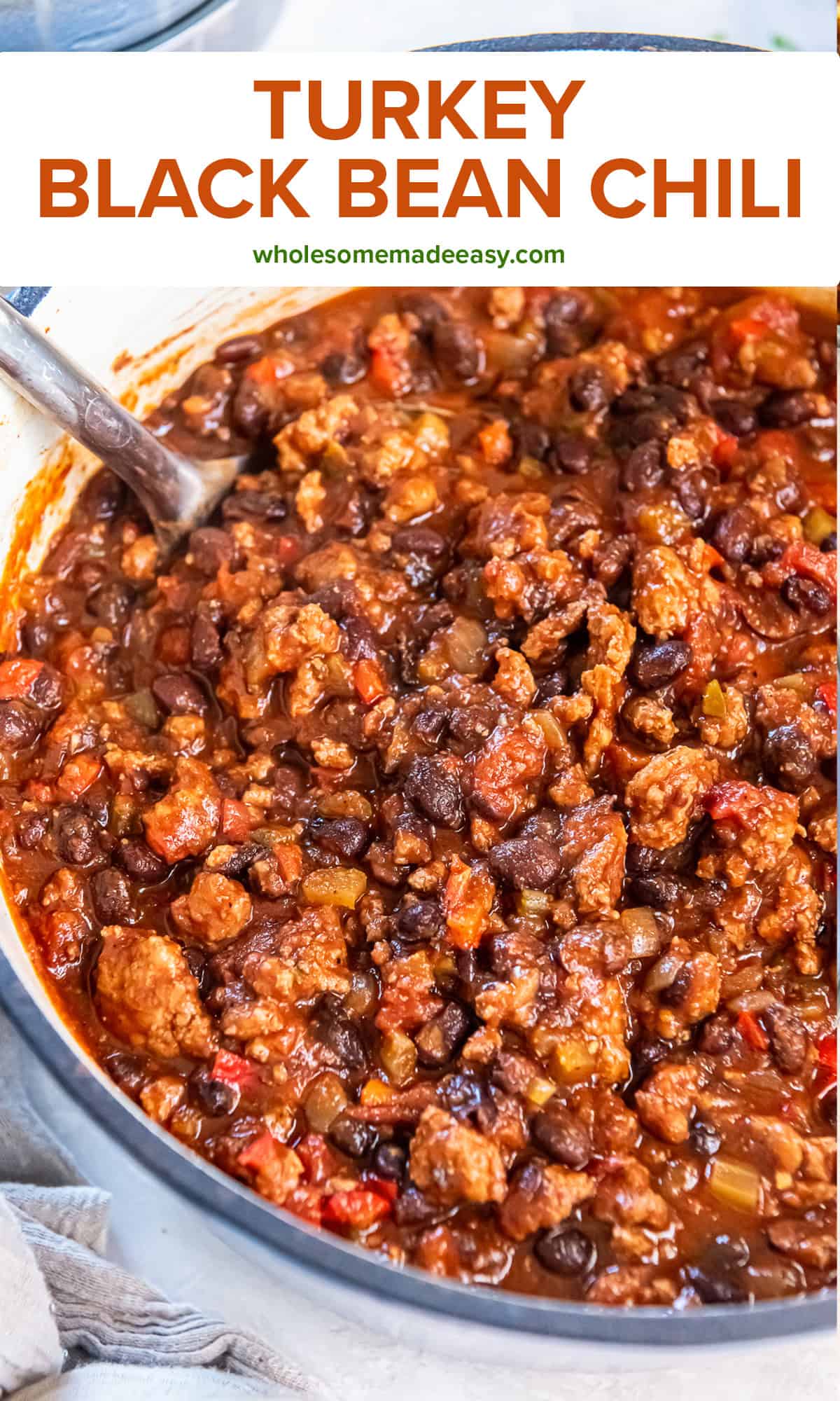 A spoon resting in a pot of turkey black bean chili with rich red sauce and hearty mix of beans, turkey, and vegetables with text overlay.