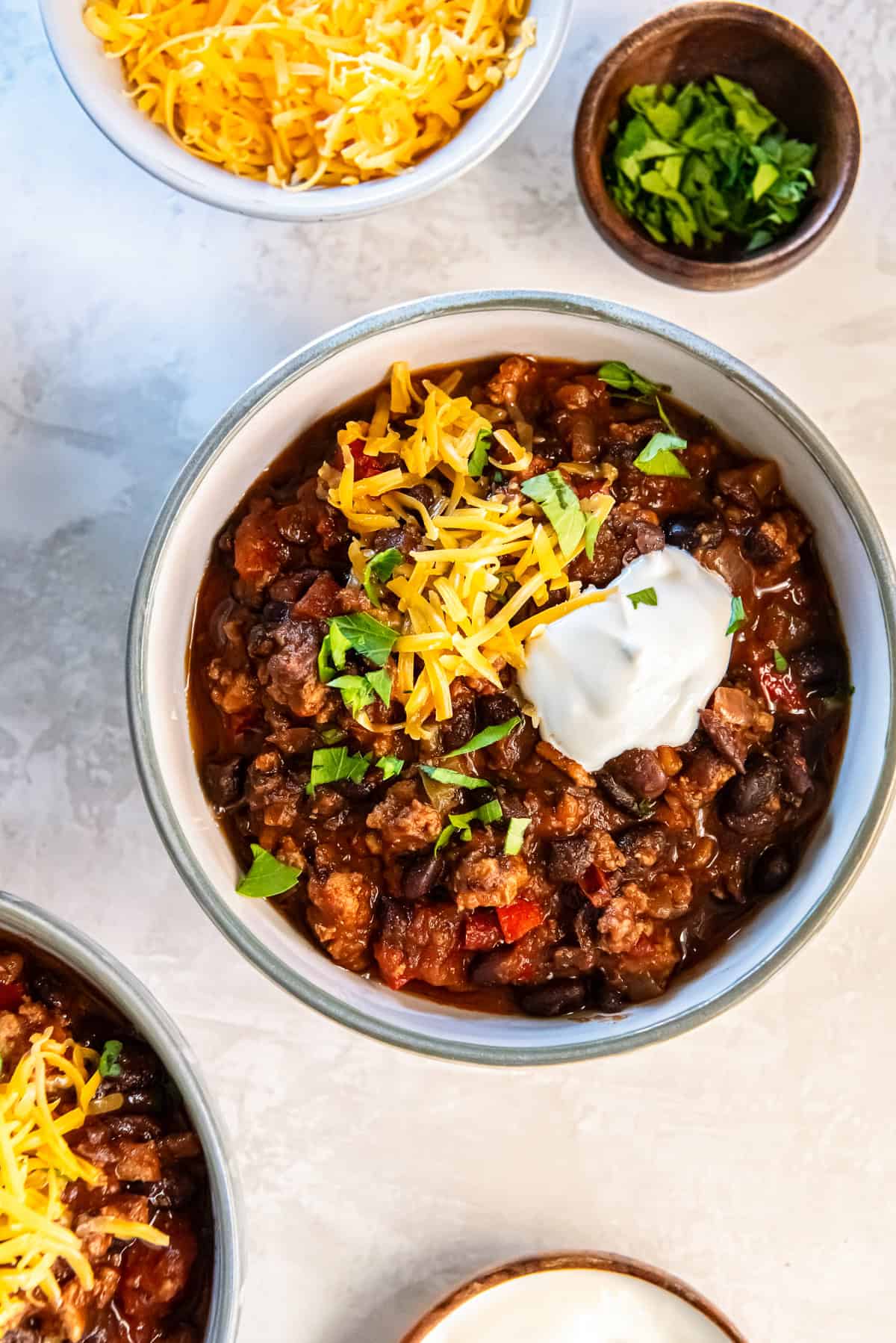 A bowl of turkey black bean chili surrounded by bowls of cheese, sour cream, and cilantro.