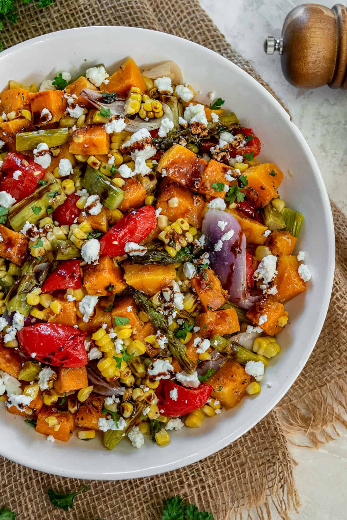 Colorful roasted fall harvest salad in a white bowl filled with roasted butternut squash, corn kernels, asparagus, red peppers, and red onion, finished with crumbled goat cheese and a drizzle of balsamic glaze.
