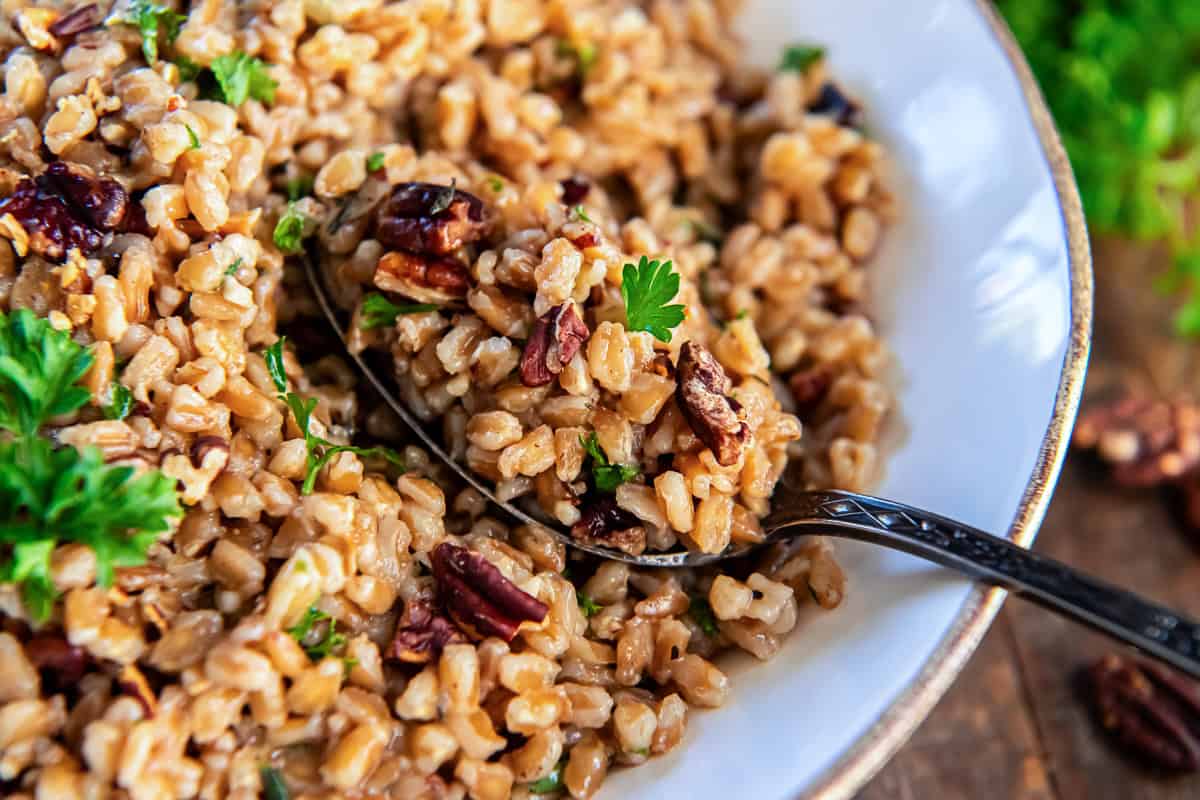A spoon scooping farro pilaf from a white bowl.