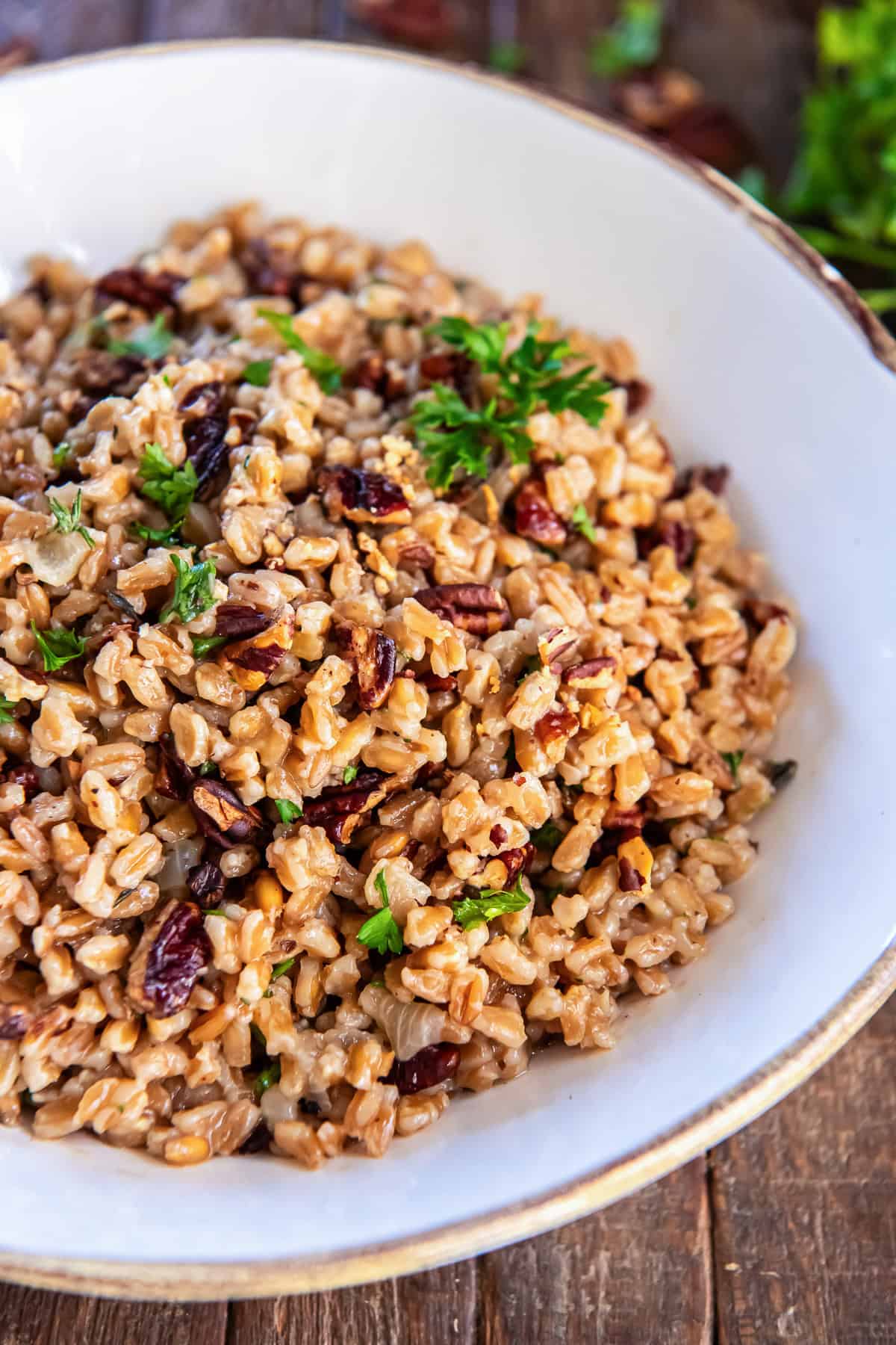 Farro pilaf with toasted pecans and fresh parsley served in a white bowl on a rustic wooden backdrop.
