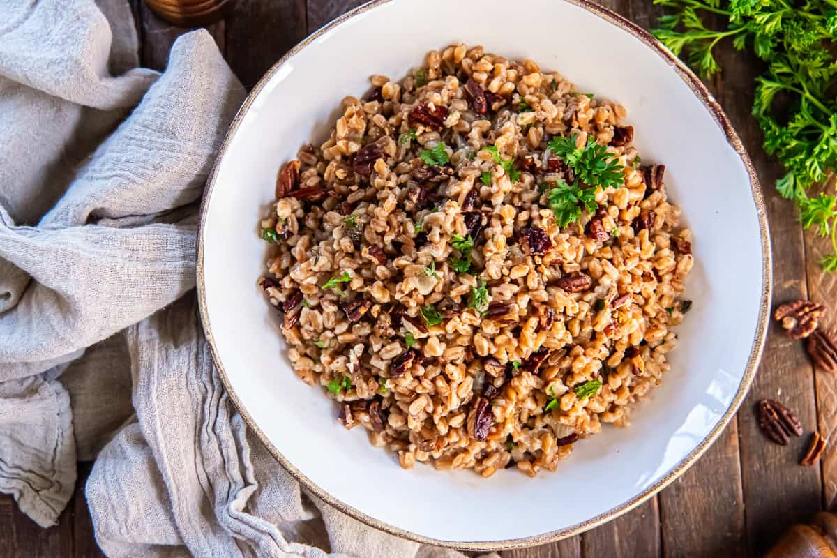 Farro pilaf with toasted nuts in a white bowl next to a beige kitchen cloth.