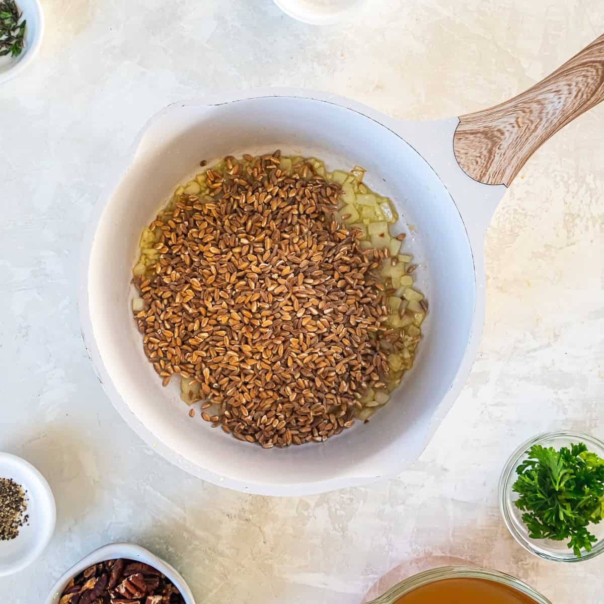Onions and farro in a white saucepan.