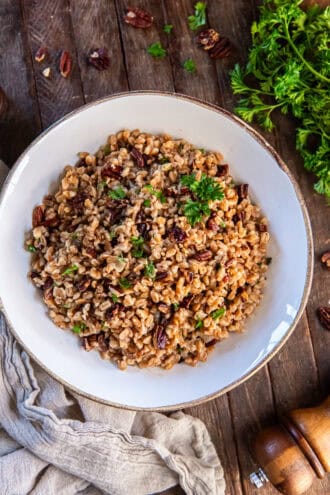 Warm farro pilaf mixed with toasted nuts and herbs, garnished with parsley.