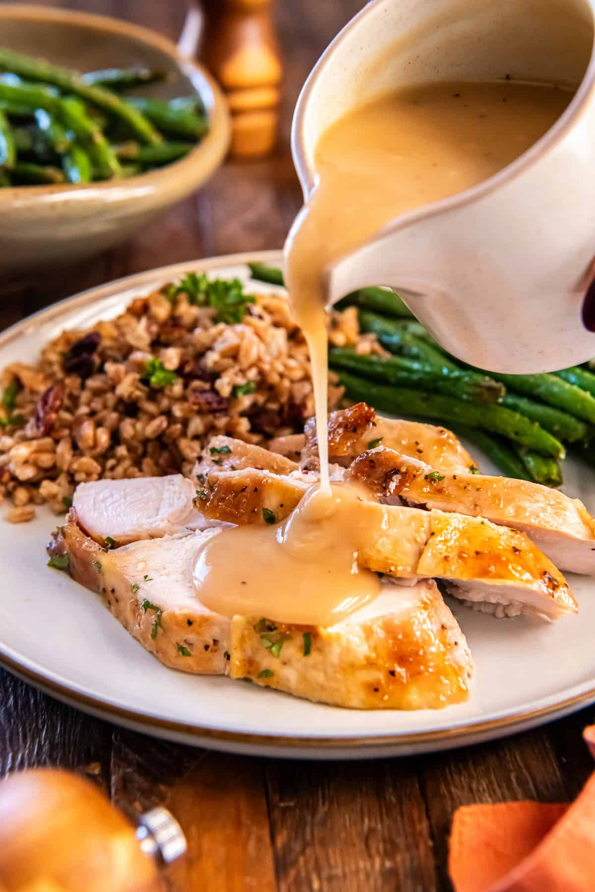 Maple glazed turkey breast sliced and served with pan gravy being poured over the top, with green beans and a grain side on the plate.