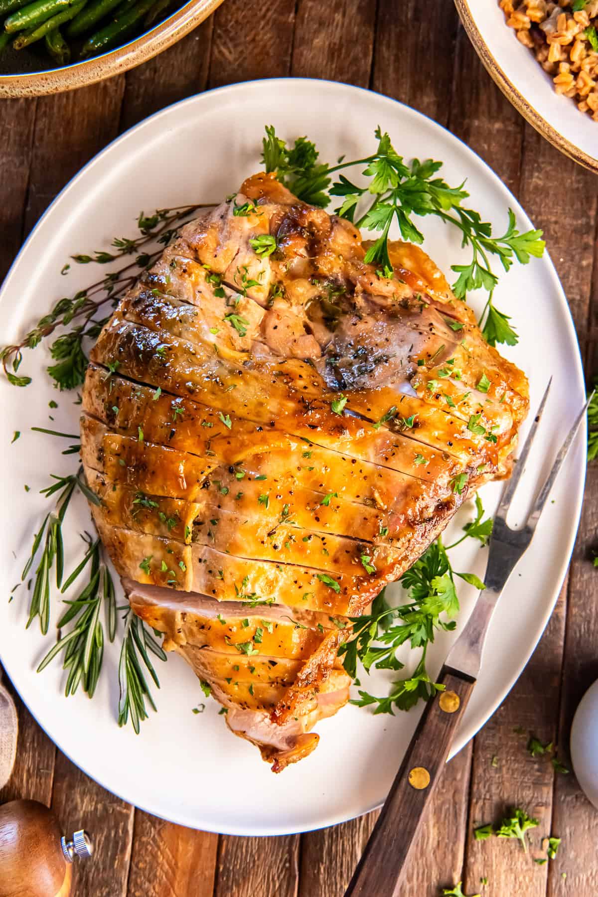 Sliced maple glazed turkey breast arranged on a platter with fresh herbs and serving knife.
