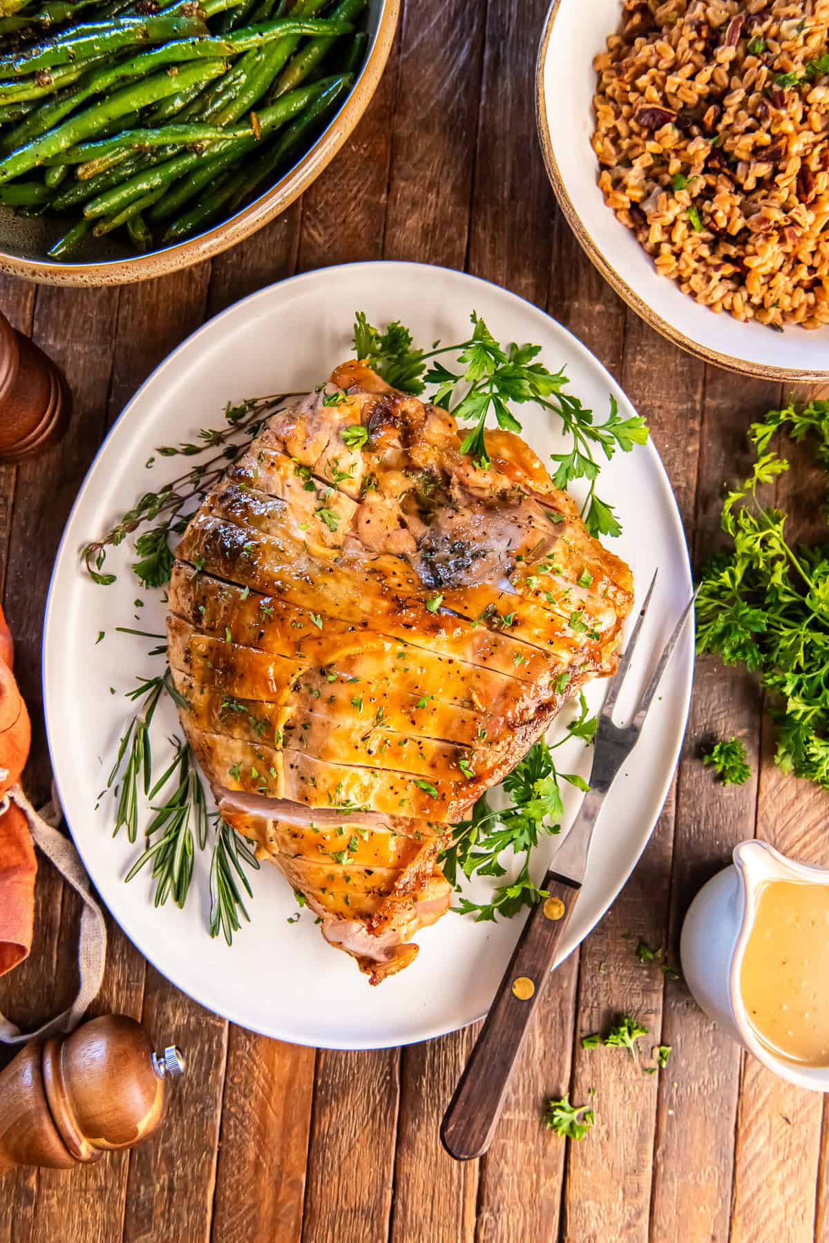 Maple glazed turkey breast served on a platter surrounded by green beans, a grain side, and a pitcher of gravy.