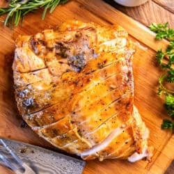Maple glazed turkey breast sliced on a wooden cutting board with fresh herbs, a carving knife, and gravy nearby.