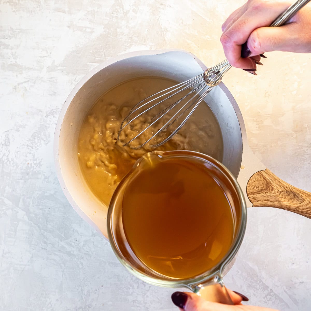 Whisking chicken broth into reserved turkey drippings in a saucepan to build the gravy.