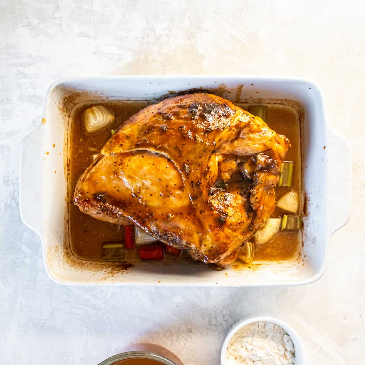 Roasted maple-glazed turkey breast resting in a baking dish with onion, carrot, celery, and pan juices.