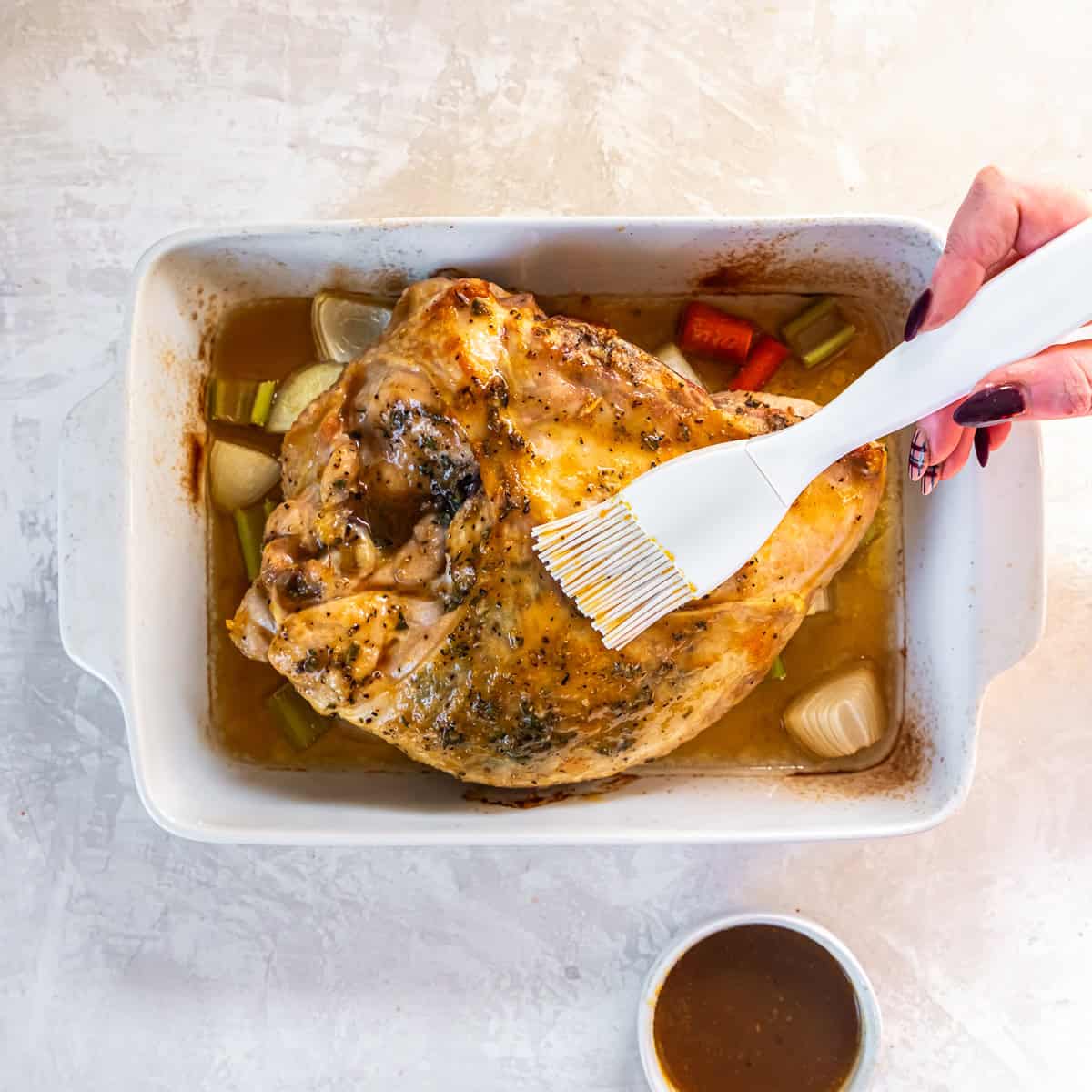 Basting a roasted turkey breast with maple-Dijon glaze in a baking dish with vegetables and broth.