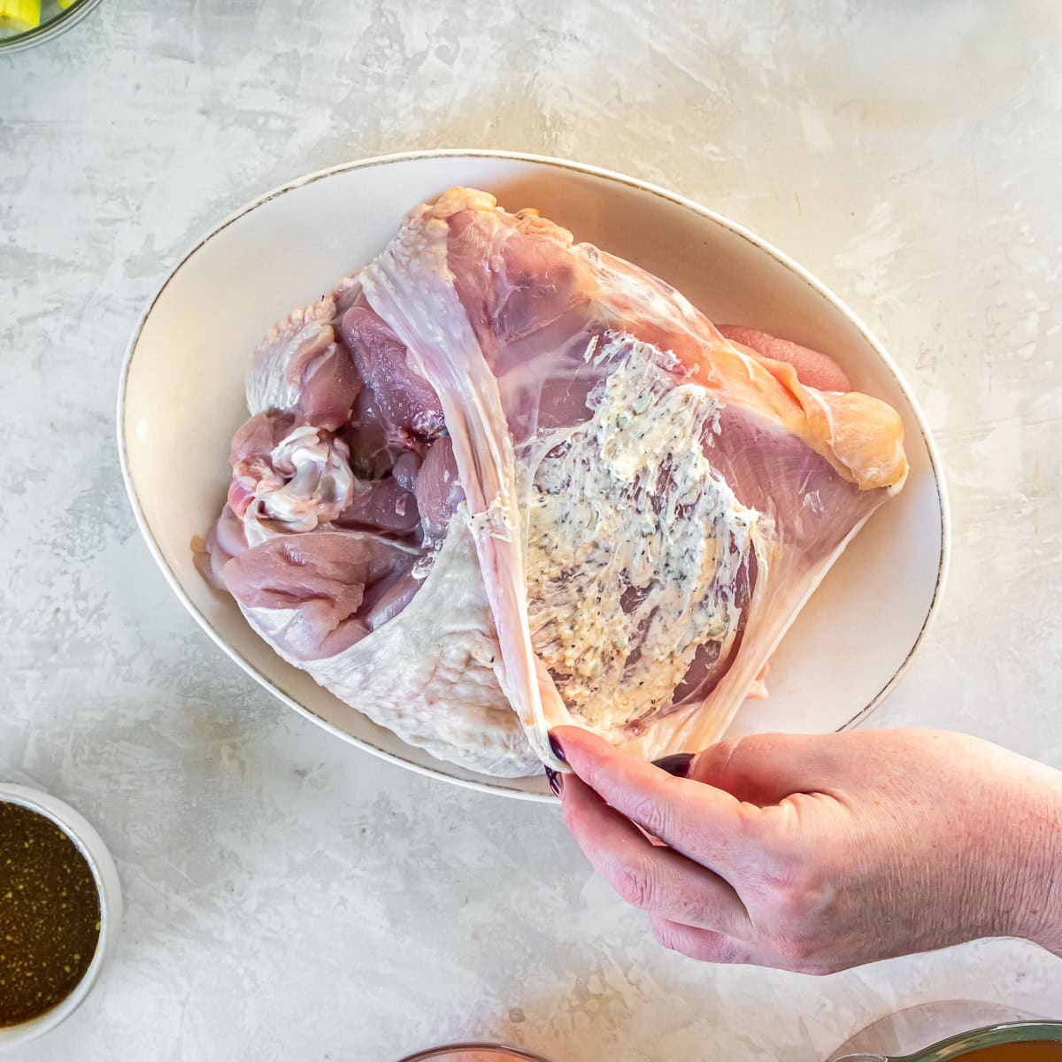Separating the skin from a raw turkey breast to spread herb butter underneath.