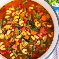 Vegetable protein pasta soup in a Dutch oven with cannellini beans, curly mac protein pasta, carrots, zucchini, green beans, tomatoes, and spinach in a tomato broth, garnished with fresh parsley.