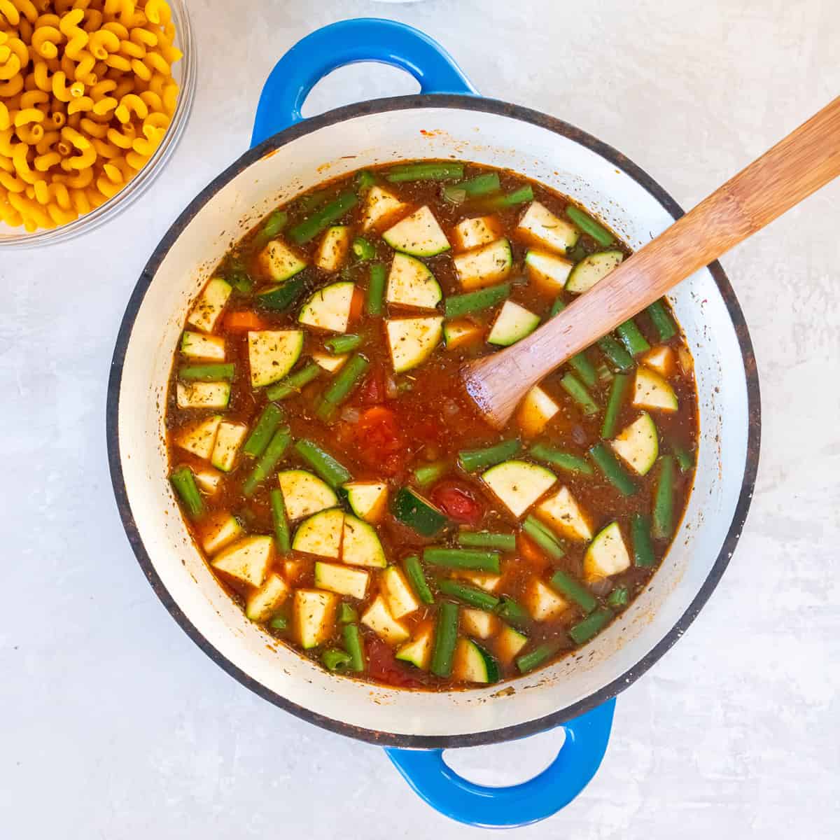 Zucchini and green beans simmering in a tomato broth with Italian seasoning in a Dutch oven.