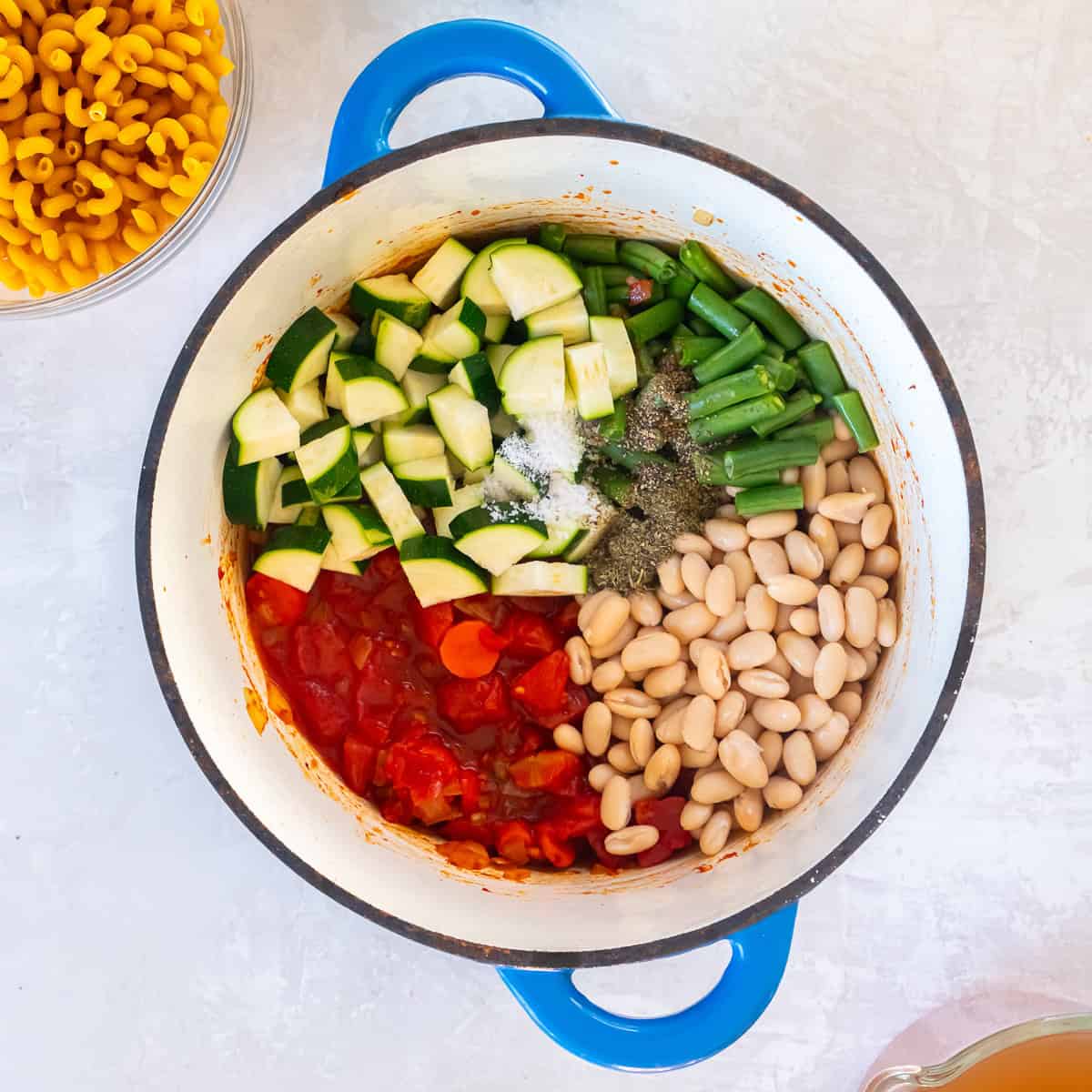 Zucchini, green beans, cannellini beans, diced tomatoes, and Italian seasoning added to a pot of soup base before simmering.
