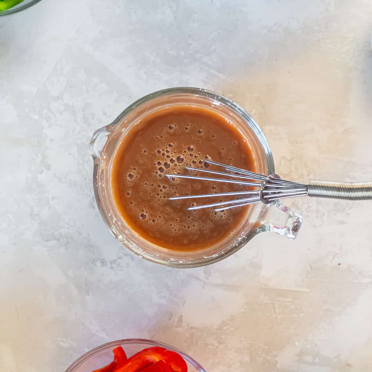 Sweet and sour sauce in a measuring cup with a whisk.