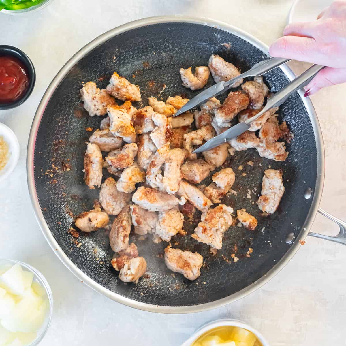 Cornstarch-coated pork tenderloin chunks browning in a skillet until lightly golden.