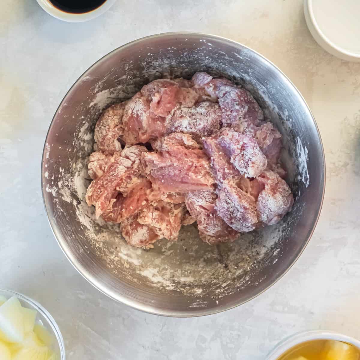 Pork tenderloin chunks coated with spices and cornstarch in a mixing bowl, ready to be browned.