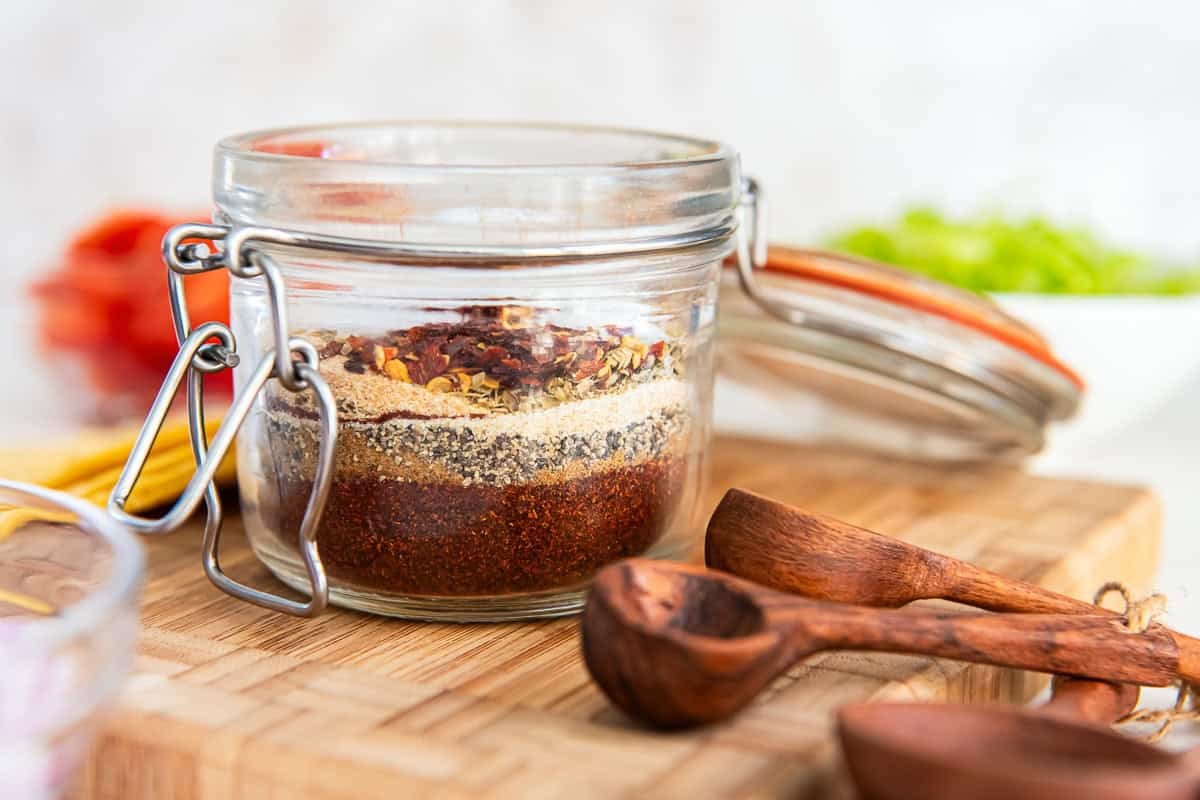 Layered ingredients for homemade low sodium taco seasoning in a glass jar on a cutting board.