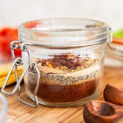 Layered ingredients for homemade low sodium taco seasoning in a glass jar on a cutting board.
