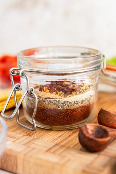 Layered ingredients for homemade low sodium taco seasoning in a glass jar on a cutting board.